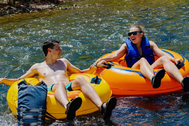Two river tubers in orange and yellow river tubes, male and female , floating in calm waters while holding hands