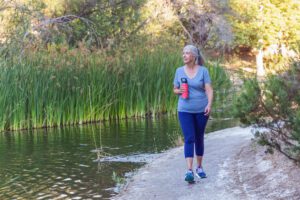 55+ Woman walking on outdoor footpath holding water bottle